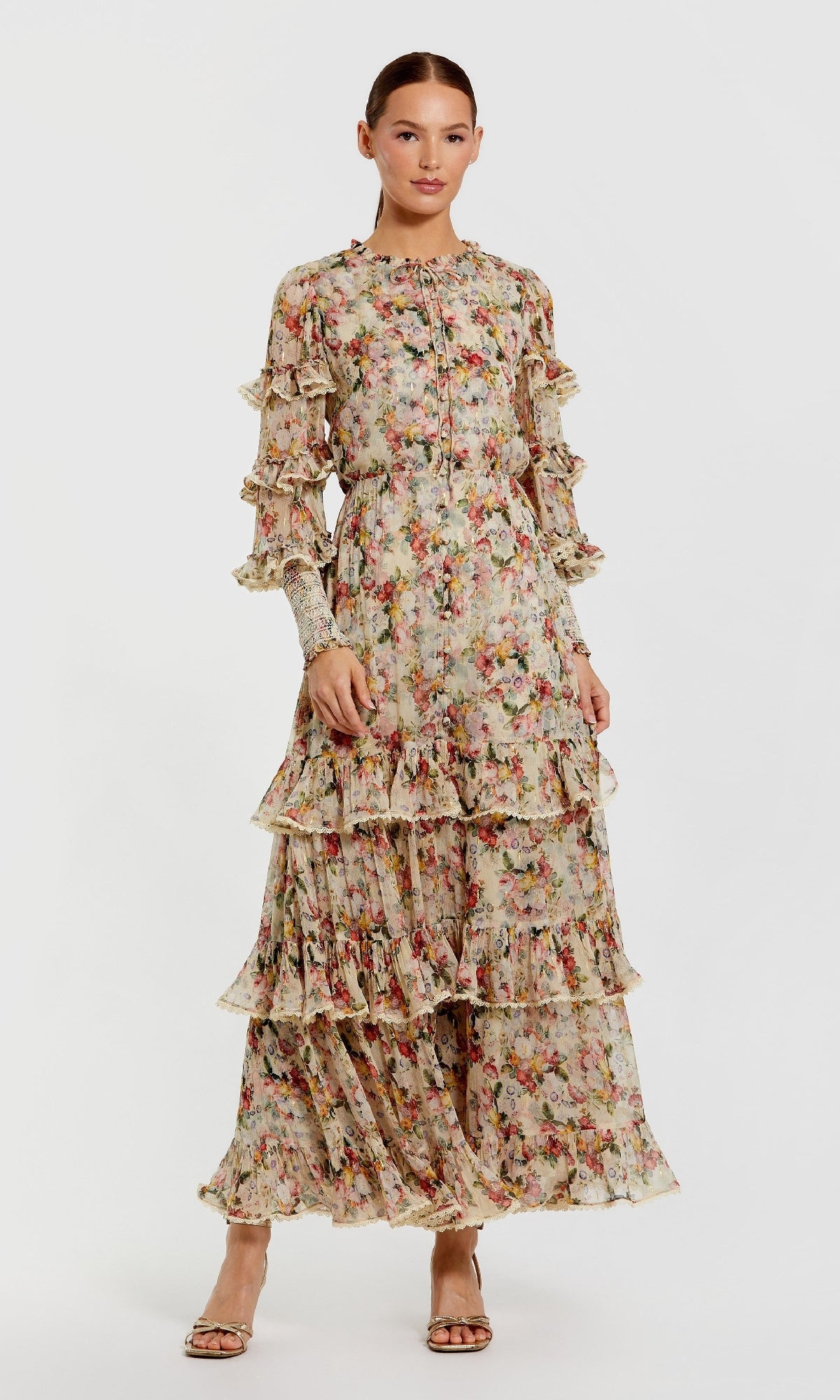 A woman models the Mac Duggal 8334 Long Sleeve Ruffle Formal Dress with a tiered floral-print design and ruffle details, paired with open-toe heels, against a plain white background.